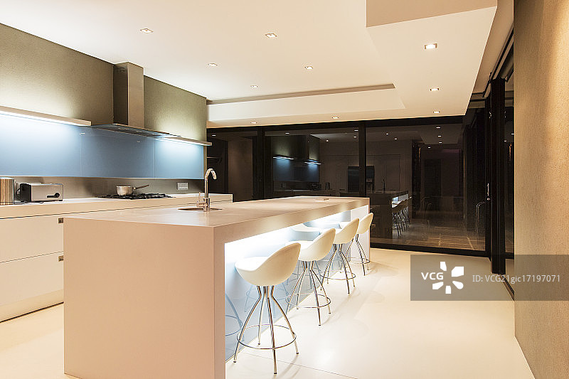 现代白色厨房，厨房岛和凳子在晚上照明图片素材