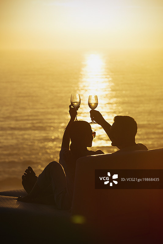 一对夫妇在阳台上举杯，欣赏着宁静的日落海景图片素材