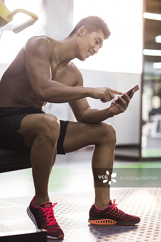 年轻男子坐在健身房使用手机图片素材