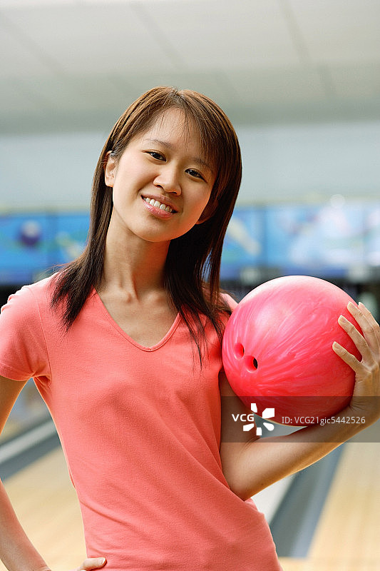 一个女人在保龄球馆拿着保龄球，手放在屁股上图片素材