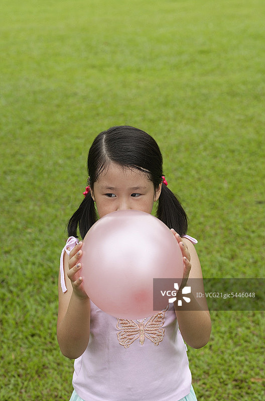 女孩站在草地上，吹起粉红色的气球图片素材