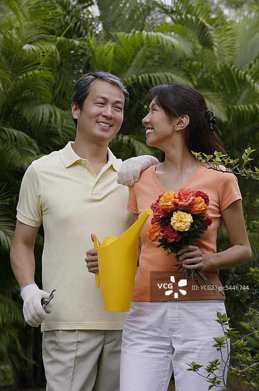 一对夫妇在花园里，女人拿着花束和喷壶，对着旁边的男人微笑图片素材