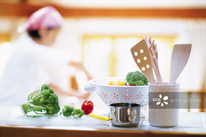 厨房台子上的滤锅里的新鲜蔬菜，背景是一个人在做饭图片素材