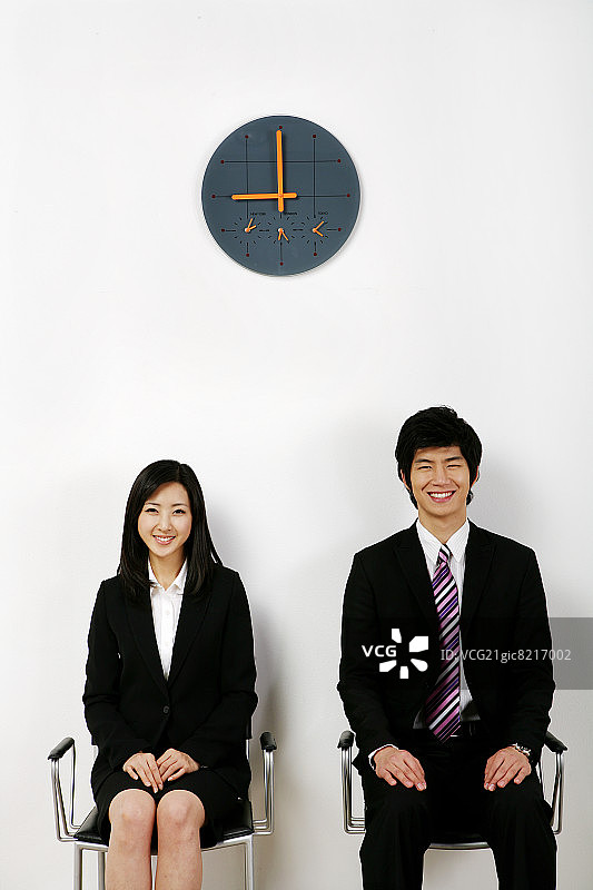 商人和女商人坐在椅子上，面带微笑，墙上挂着时钟图片素材