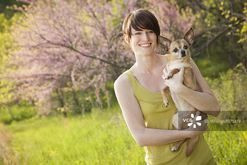 初夏的草地上，一个年轻女子抱着一只狗图片素材