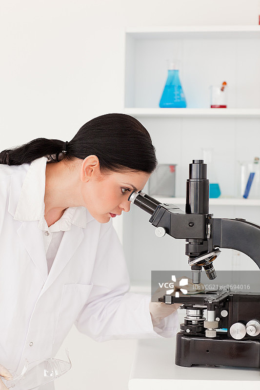 在实验室里通过显微镜观察的黑发女科学家图片素材