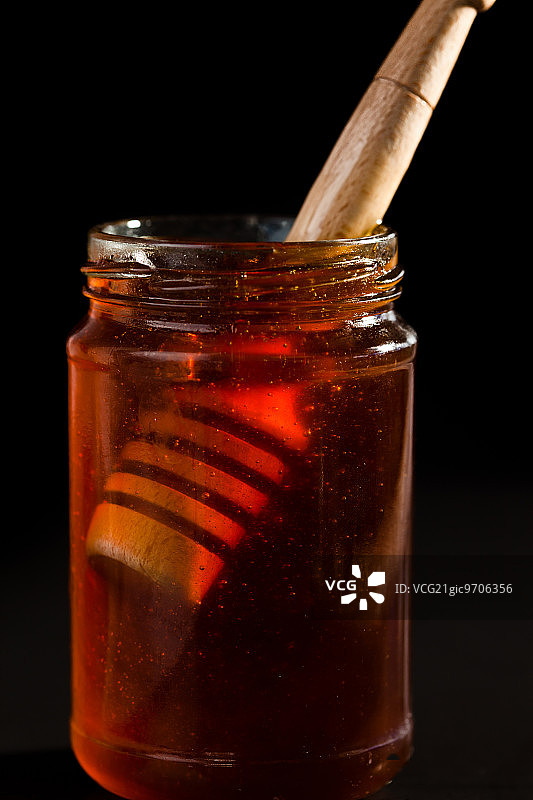 蜂蜜勺在一个蜂蜜罐子在一个黑色的背景图片素材