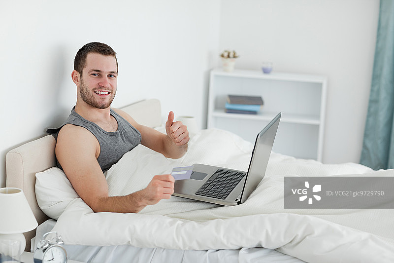 快乐的男人在卧室里竖起大拇指在网上购物图片素材