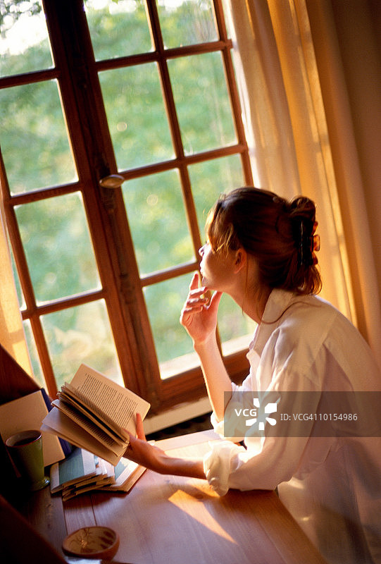 年轻女子在阳光照耀下的窗户旁阅读图片素材
