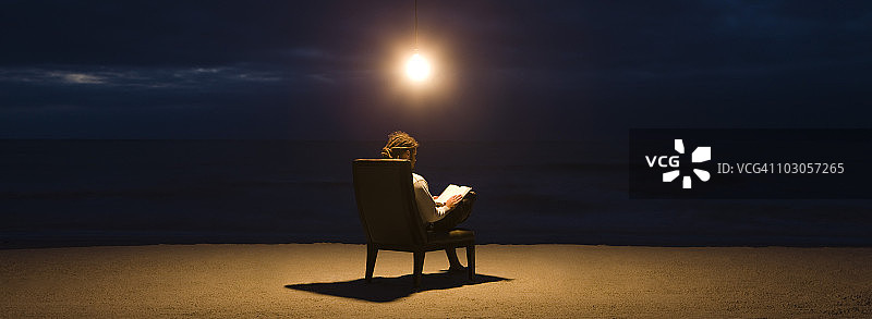 晚上在海滩上，一个人坐在电灯泡下的椅子上看书图片素材