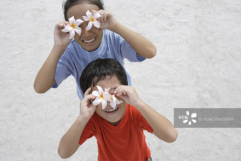 两个孩子举着两朵鸡蛋花在他们眼前的高角度视图图片素材