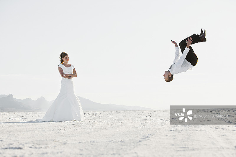 美国，犹他州，博纳维尔盐滩，新娘观看新郎表演后空翻在沙漠图片素材