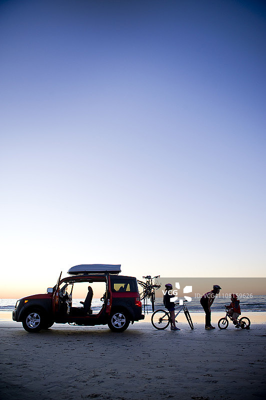 家庭在海滩上，汽车和自行车，日落图片素材