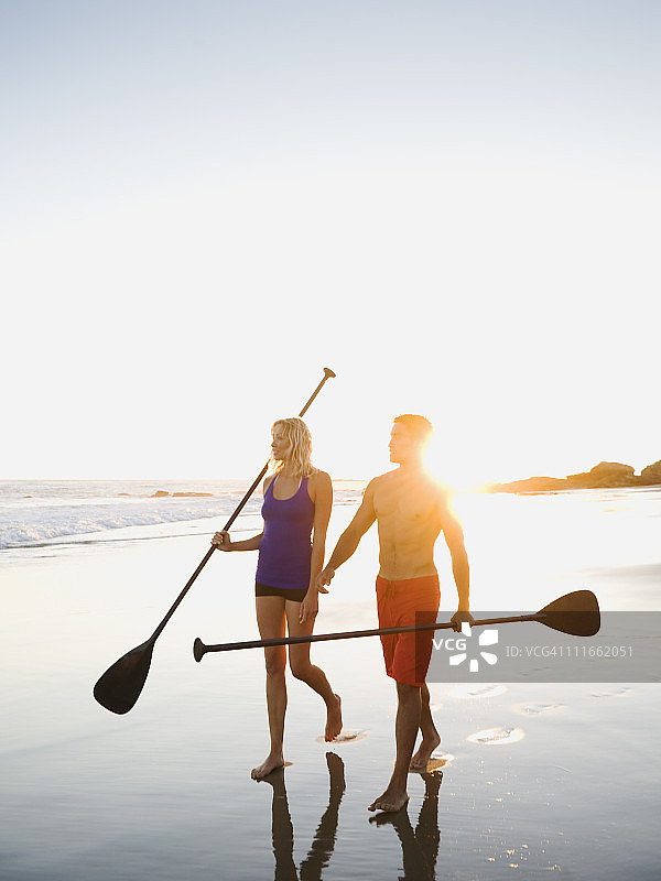 一对夫妇在海滩上散步，拿着划桨图片素材
