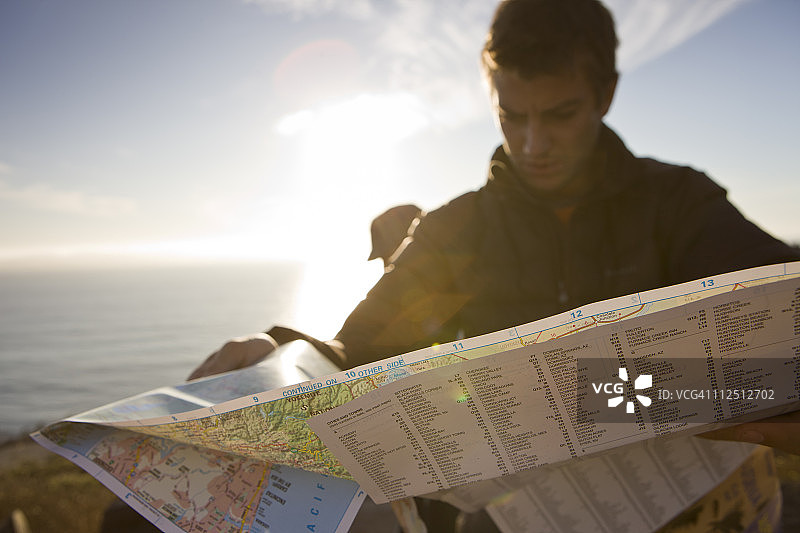 一个男人在看地图，后面是海洋。图片素材