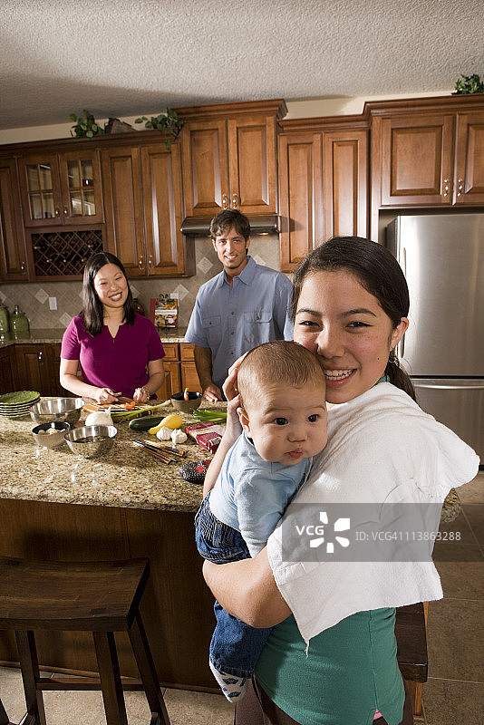 女孩抱着孩子，妈妈在后台准备晚餐图片素材