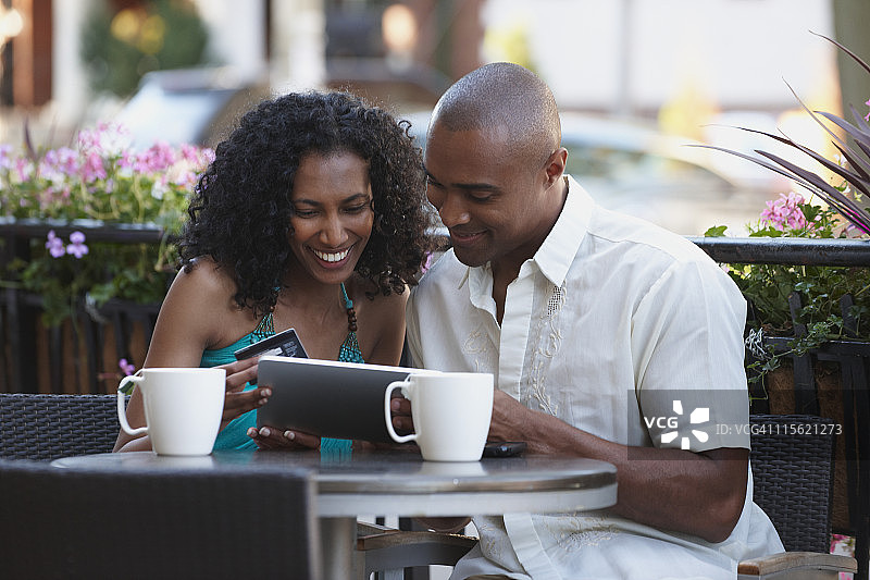 夫妇与信用卡在咖啡馆看数字平板电脑一起图片素材