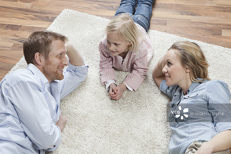 德国，巴伐利亚，慕尼黑，父母和女儿躺在地毯上，微笑图片素材