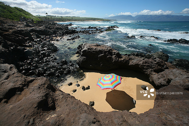 色彩鲜艳的沙滩伞在一个沙圈周围的熔岩岩石旁边的海洋。图片素材