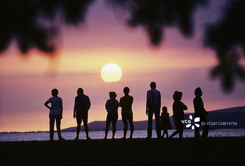 一群人的剪影站在海滩上看美丽的日落。图片素材