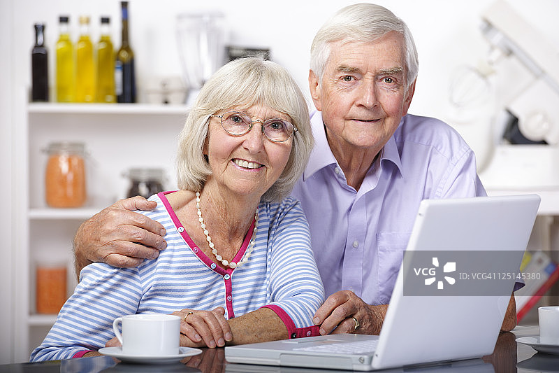 老年夫妇在家庭厨房里使用笔记本电脑的肖像图片素材
