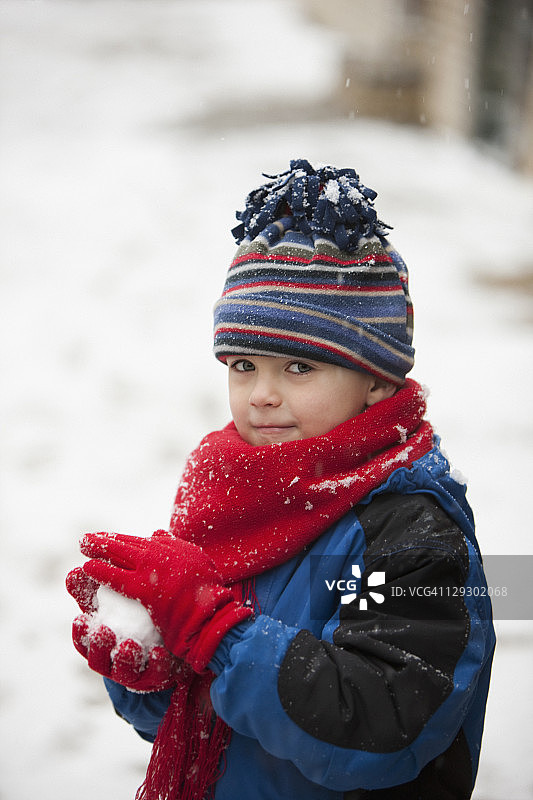 白种人男孩戴着帽子和围巾滚雪球图片素材