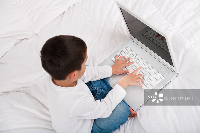 小男孩在床上用笔记本电脑图片素材