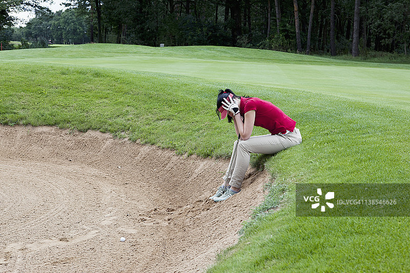 一个女高尔夫球手坐在沙坑的边缘，双手抱头图片素材