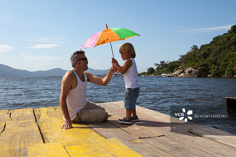 父亲和儿子在码头上撑着太阳伞图片素材
