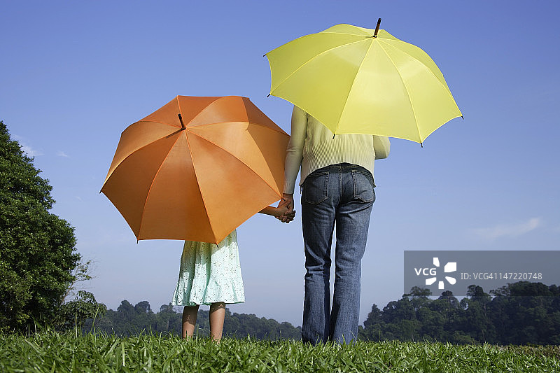 一个女人和一个女孩站在黄色和橙色的雨伞前图片素材