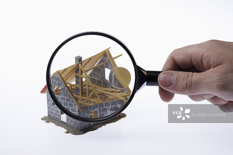 一只手拿着放大镜对着一个部分搭建的微型房屋模型图片素材