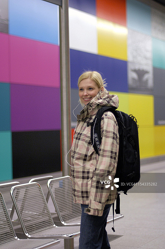 微笑的年轻女子背包和耳机在地铁站图片素材