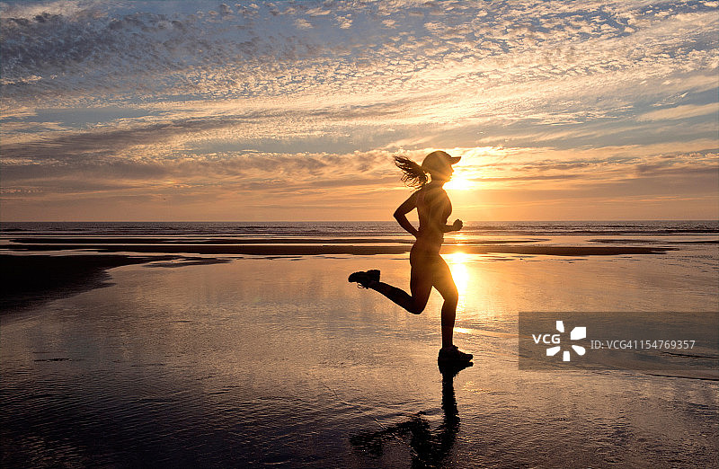 日出时在海滩上跑步的女人图片素材