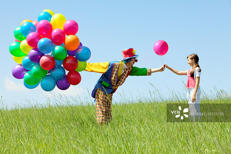 小丑用气球捧花送给田野里的一个女孩图片素材