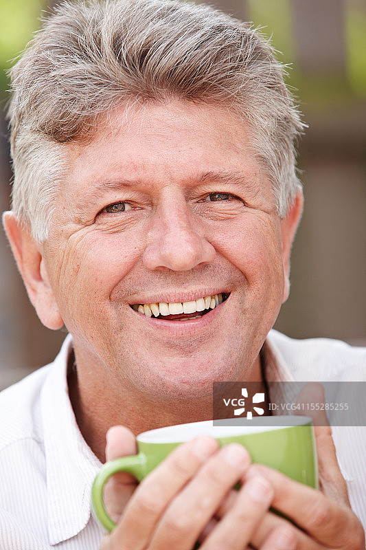 老人在户外喝着绿杯子里的咖啡图片素材