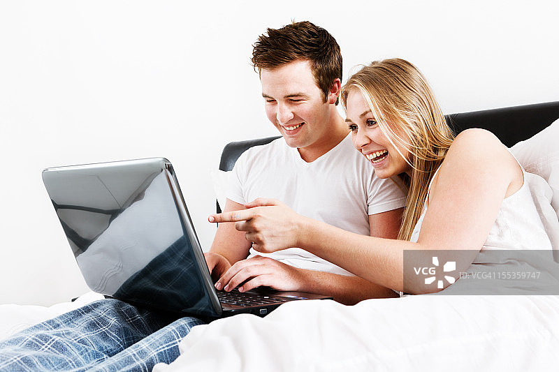 幸福的年轻夫妇在床上对着笔记本电脑屏幕微笑图片素材