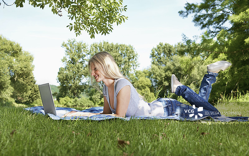 德国，科隆，年轻女子在草地上使用笔记本电脑图片素材