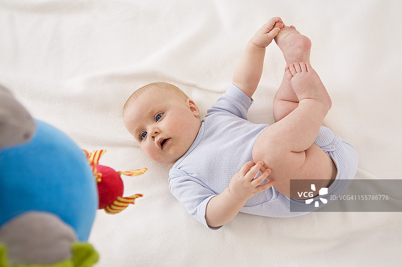 女婴抱着脚躺在婴儿毯上图片素材