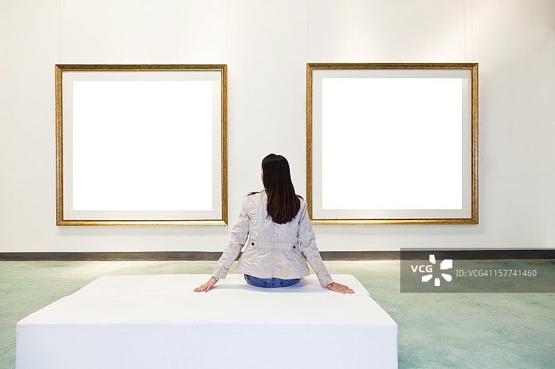 一个女人在画廊里看着白色的画框图片素材