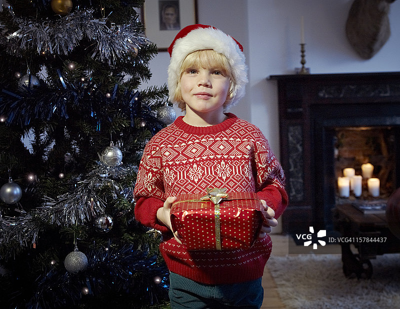 孩子拿着圣诞礼物在树旁。图片素材