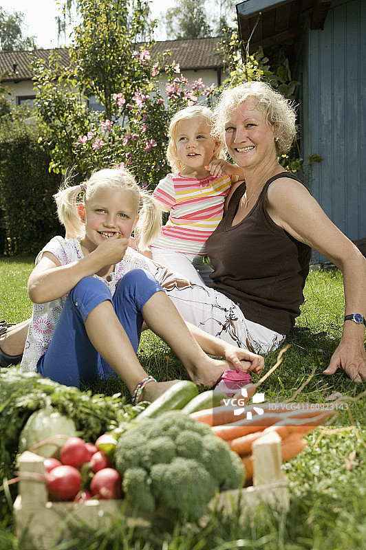 德国，巴伐利亚，奶奶和孩子们坐在花园里，蔬菜在前景图片素材