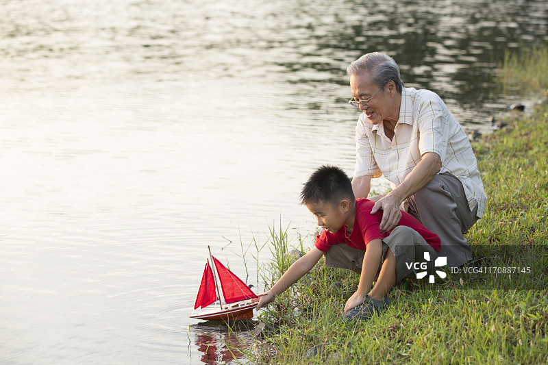 爷爷在湖边帮孙子玩模型船图片素材