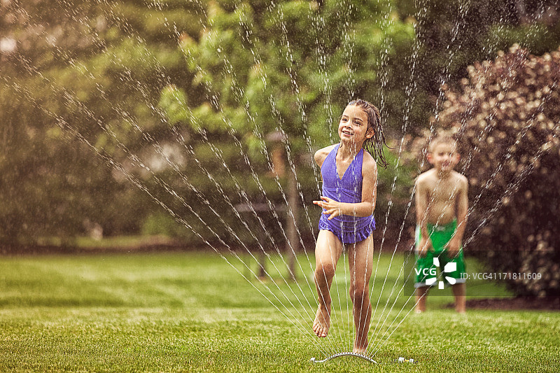 女孩和男孩跑过花园洒水器图片素材