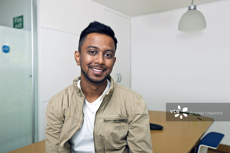 年轻的印度男子在他的办公室对着镜头微笑图片素材