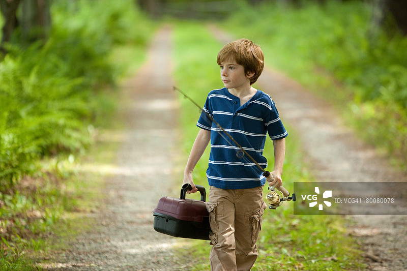 一个男孩拿着钓竿走在乡间小路上图片素材