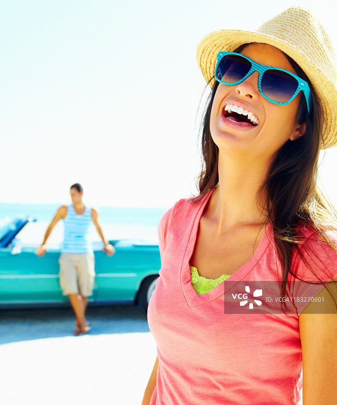 快乐的年轻女子戴着太阳镜，背景是男子图片素材