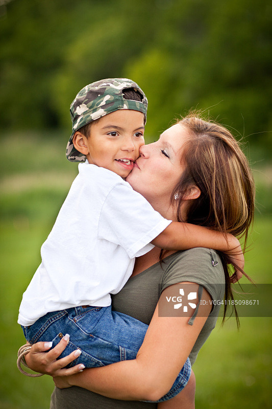 快乐，年轻的母亲在户外拥抱和亲吻她的儿子图片素材