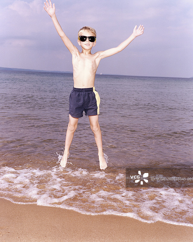 男孩(6-8岁)戴着太阳镜在海滩上跳起来图片素材