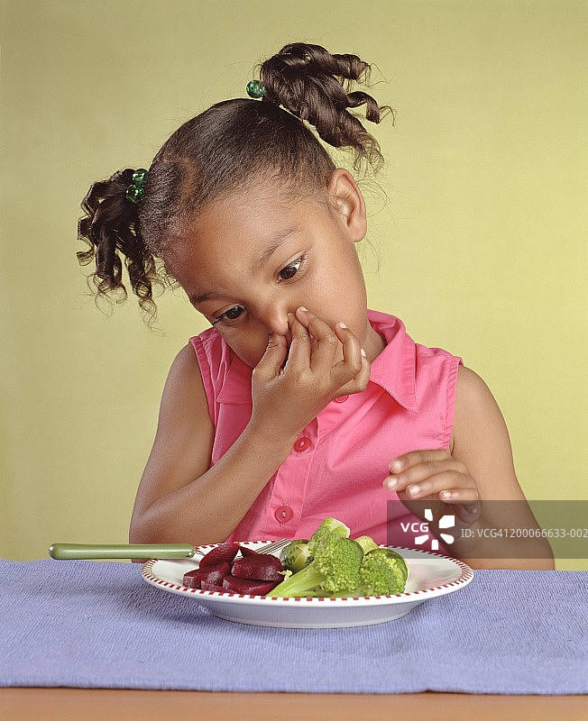 4-6岁的女孩捏着鼻子看一盘蔬菜图片素材