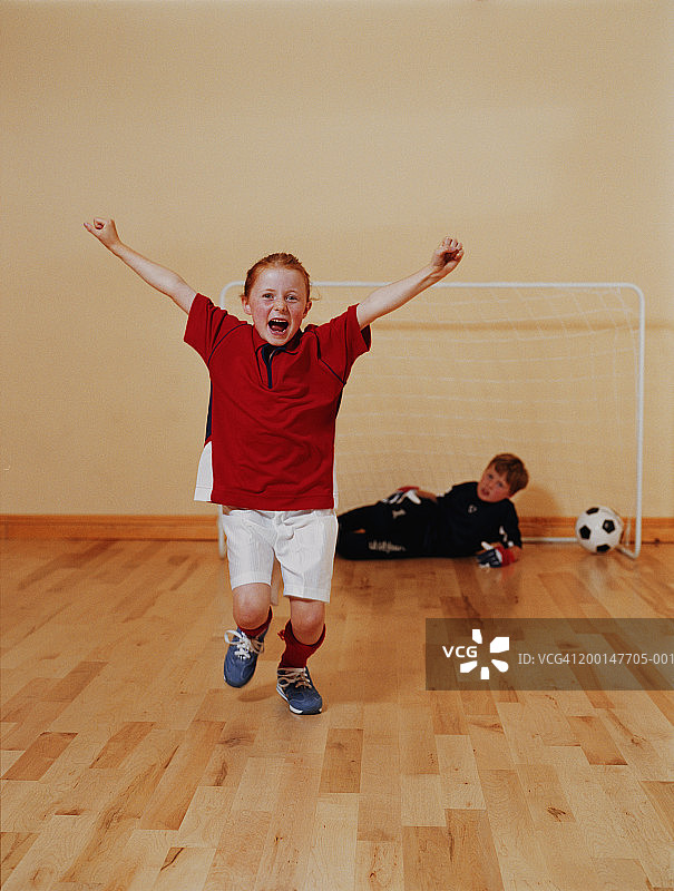 女孩(6-8)，举起手臂，在男孩(8-10)前面防守足球球门图片素材